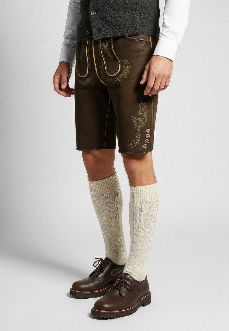 Bruine leren shorts met geborduurd bloemenpatroon, gouden accenten, zijzakken en knopen. Gecombineerd met crème knielange sokken en donkere schoenen.