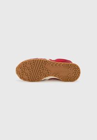 Semelle d'une basket rouge Converse avec une bande de roulement en caoutchouc beige présentant des motifs en zigzag et flèche ainsi que le logo Converse.