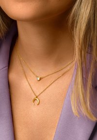Goldbeschichtete Halsketten mit einem runden Anhänger und einem Pendant. Eine hat einen kleinen Edelstein, während die andere ein mondförmiges Design aufweist.