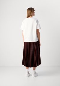 Hvit bomulls t-skjorte, løs passform, paret med en dyp burgunder plisserte skjørt og hvite sneakers, båret med ankelsokker.