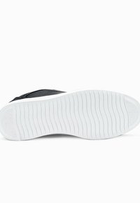 Sneaker nera con tomaia testurizzata, dotata di una suola in gomma bianca con un motivo a ondulazione. Il design è semplice e funzionale.