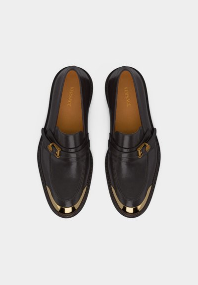 Μαύρα δερμάτινα loafers με χρυσές μεταλλικές λεπτομέρειες στα δάχτυλα και πλαϊνά τοκάκια, με την ετικέτα Versace εσωτερικά.