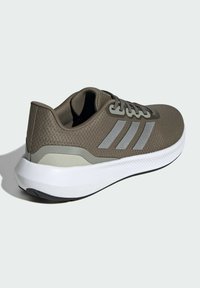 Zapatilla deportiva verde con parte superior sintética texturizada, acentos grises y tres rayas. Presenta una mediasuela blanca y una suela negra.