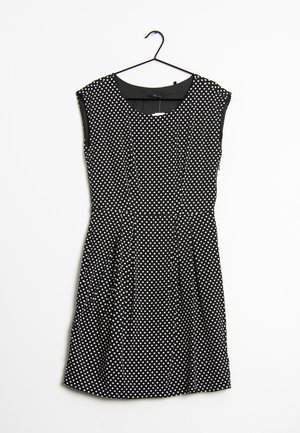Schwarzes ärmelloses Kleid mit weißen Punkten, tailliert, plissierter Rock, an einem schwarzen Kleiderbügel vor weißem Hintergrund hängend.