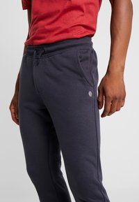 Marina blå mjukisbyxor med elastisk midja, sidofickor och en liten logotypapplikation. Mjukt tyg med en slät textur.