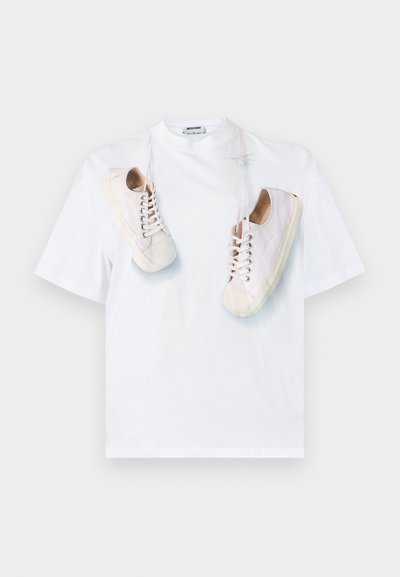 Λευκό βαμβακερό t-shirt με σχέδιο γραφικών που απεικονίζει μπεζ αθλητικά παπούτσια με κορδόνια. Σχέδιο με στρογγυλή λαιμόκοψη και κοντά μανίκια, απλή και καθαρή αισθητική.