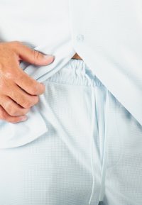 Haut à boutons texturé bleu clair et pantalon à taille élastique assorti. Les éléments notables incluent un cordon de serrage réglable et un motif à fines mailles.