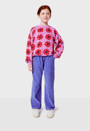 Rosa Sweatshirt mit rotem Blumenmuster und schwarzen Mitte; kombiniert mit blauen Cordhosen; weiße Sportschuhe; Frontalansicht eines Kindes.