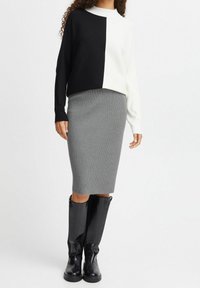 Black and white ribbed sweater with a high neckline, paired with a fitted gray ribbed skirt and knee-high black boots.