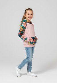 Jasnoróżowa bluza z kapturem z rękawami w kwiatowy wzór, kieszenią kangurka, w połączeniu z niebieskimi dżinsami i białymi trampkami. Gładka tkanina, swobodny krój.