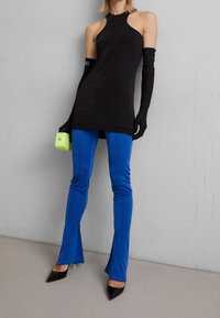 Czarny top bez rękawów, niebieskie dzwonowate legginsy, czarne szpilki w szpic oraz mała neonowo-zielona torebka o gładkiej fakturze.