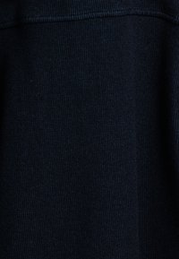 Close-up van donkerblauwe gebreide stof die de gedetailleerde textuur en het stikpatroon toont.