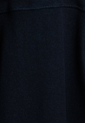 Close-up van donkerblauwe gebreide stof die de gedetailleerde textuur en het stikpatroon toont.