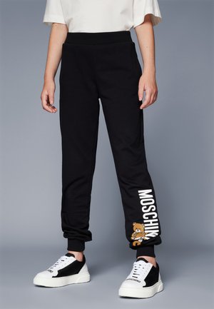 Pantaloni da tuta neri con vita e polsini a coste, caratterizzati da testo stampato bianco "MOSCHINO" e una grafica di orsetto sulla parte bassa della gamba sinistra.
