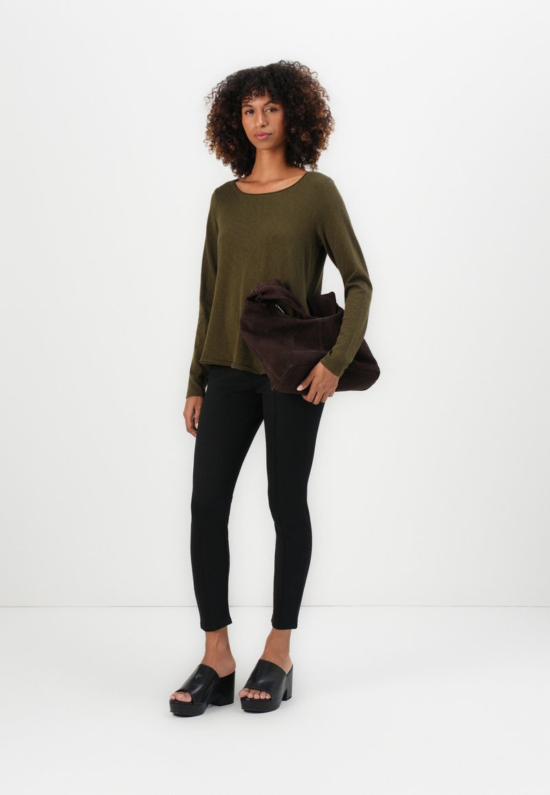 Oliwkowa bluzka z długim rękawem, czarne dopasowane spodnie oraz ciemnobrązowa miękka torebka. Modelka nosi czarne klapki na platformie. Minimalistyczny design, gładkie tekstury.