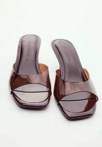 Paire de sandales slides transparentes marron avec bouts carrés et semelles plates placées côte à côte sur une surface blanche.