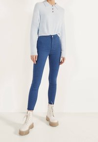 Light blue fuzzy sweater with three buttons, paired with high-waisted blue checkered leggings and white lace-up platform boots.