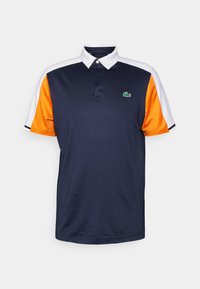 Marinblå piké med orange och vita ärmar. Har en klassisk krage, tvåknapplikation och en liten grön krokodil-logga.