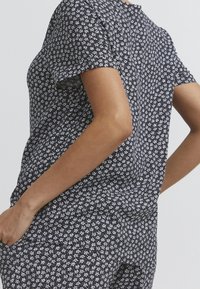 Top corto a maniche corte in bianco e nero con scollatura rotonda e vestibilità rilassata, realizzato in tessuto leggero, caratterizzato da un piccolo motivo su tutta la superficie.