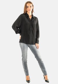 Camisa negra de botones con un bolsillo, corte holgado, mangas largas. Combinada con jeans azules desgastados y tacones altos negros. Textura suave.