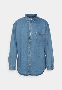 Camicia azzurra in denim a maniche lunghe, con taschino sul petto e colletto classico, esposta su uno sfondo bianco.