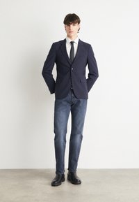 Tumed blazer, milledega, ühel nööbil kinnitamine ja kaks eesmist taskut. Koos tumedate teksade ja mustade chelsea saapatega.