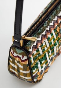 Mała torebka z wielokolorowymi koralikowymi wzorami geometrycznymi, czarnym skórzanym paskiem i złotym zamkiem błyskawicznym na jasnym tle.