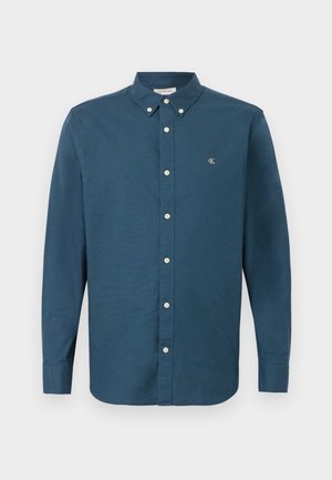 Mørkeblå langermet skjorte i bomull med knappestolpe på kragen, hvite knapper og en liten brodert logo på brystet.