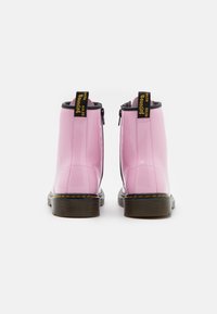 Stivaletti alla caviglia in pelle verniciata rosa con dettagli neri, chiusura con zip e linguette gialle con logo sul tallone. Suole spesse in gomma marrone texturizzata.