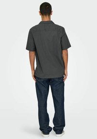 Korte mouwen, donkergroene shirt met een kraag en een rechte zoom, gecombineerd met losjes zittende blauwe jeans en witte sneakers.
