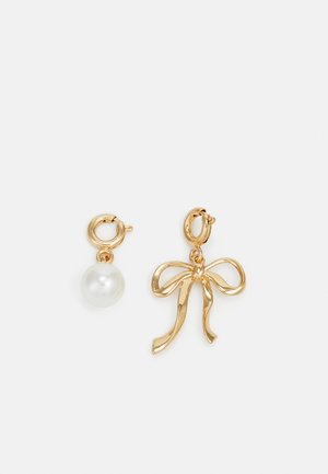Orecchini a goccia in oro con una perla tonda e un charm a forma di fiocco. La perla ha una superficie liscia, mentre il design del fiocco è elegante e lucido.