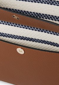 Brun läderväska med ett vävt inredning i krämfärgade och navy randigt mönster, med ett guldfärgat tryckknappslås och en texturerad utsida.