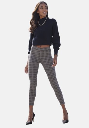 Schwarzer, gerippter, cropped Pullover, hochtaillierte Karottenleggings in Beige und Grau, glatte Textur, kombiniert mit schwarzen High Heels. Akzentuierung mit einer goldenen Kettenhalskette.