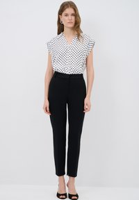 White polka dot blouse with cap sleeves, paired with black tailored pants. The outfit features a fitted silhouette and subtle pleating at the waist.