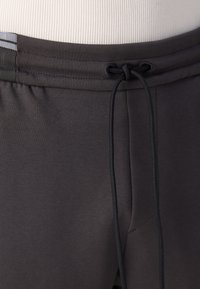 Grå atletiske shorts med snor i taljen, glat tekstur og sidelommer. Stoffet er let og strækbart.