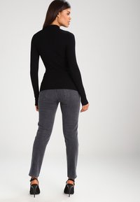 Haut à manches longues noir à côtes associé à un jean skinny gris et des escarpins noirs, vu de l'arrière, mettant en valeur la coupe et la texture de la tenue.