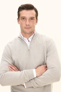 Hellgrauer Reißverschluss-Pullover mit gerippten Bündchen, kombiniert mit einem weißen Hemd mit Kragen, getragen von einem Mann mit verschränkten Armen vor neutralem Hintergrund.