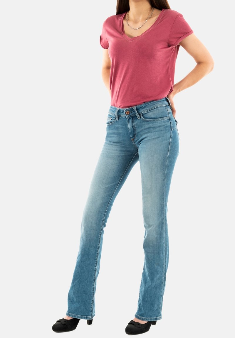 Roza majica s v-neck izrezom izrađena od mekog materijala, uparen s svijetloplavim trapericama s oblikovanim nogavicama koje imaju pet džepova i blago izblijedjelu teksturu.