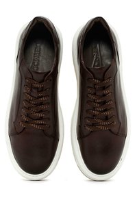 Zapatillas de cuero marrón con cordones a tono, suelas de goma blanca y costuras sutiles. Textura suave con un diseño elegante y de perfil bajo.