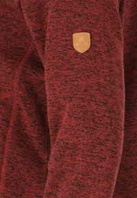 Röd texturerad hoodie med dragkedja fram, framträdande sömmar och en beige läderlogotyp på vänster ärm.
