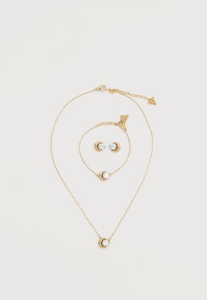 Smykkesæt i guldtone bestående af halskæde, armbånd og øreringe med halvmåne- og stjernedesign, hver dekoreret med en central klar ædelsten.