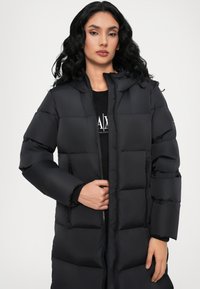 Black puffer coat with a hood, featuring a quilted design, zip closure, and side pockets. The material appears smooth and insulated.