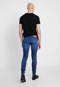 Blauwe denim skinny jeans met een leren merkpatch, gecombineerd met een effen zwart t-shirt. De outfit wordt aangevuld met zwarte boots.