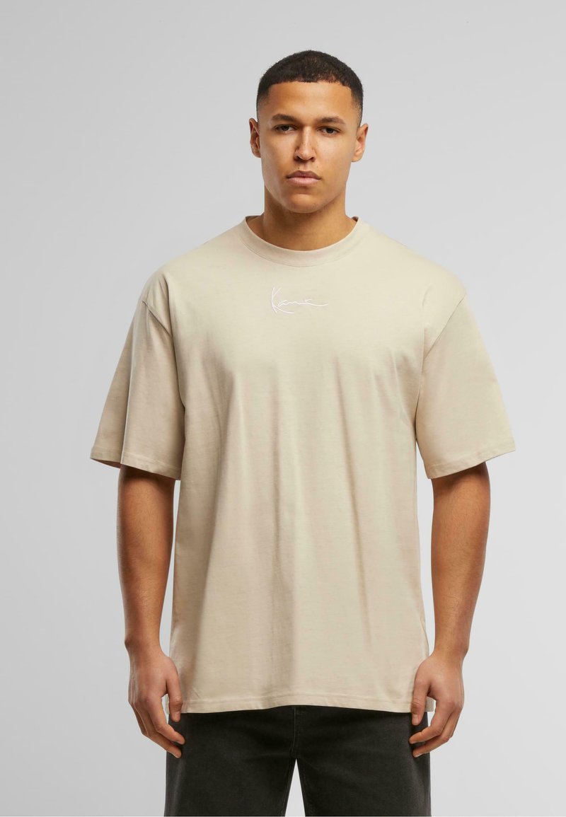 Khaki oversized t-shirt with short sleeves, round neckline, and white embroidered logo on the chest, made from soft, lightweight fabric.