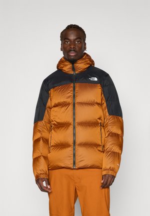 Pufferjack in verbrand oranje met zwarte accenten, met een ritssluiting, capuchon en doorgestikte ontwerp. Nylon materiaal met elastische manchetten.