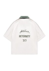 Chemise blanche à manches courtes avec col vert, manches côtelées et texte brodé "Atelier RETERNITY 7/7" dans le dos.