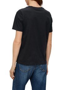 Zwarte katoenen T-shirt met korte mouwen, ronde halslijn en rechte snit, vanaf de achterkant bekeken, gecombineerd met blauwe denim jeans.