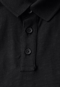 Mustapaitapusero, jossa on tekstuurinen kangas, kolme mustaa nappia ja klassinen kauluksen muotoilu. Ei näkyviä logoja tai kuvioita.