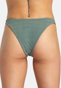 Grön bikiniunderdel gjord av texturerat tyg med rutigt mönster, med högskuren design och minimal täckning.