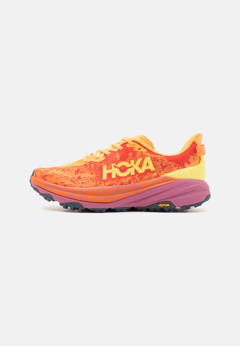 Chaussure de course HOKA de couleur orange vif et jaune avec une semelle intermédiaire violette et une semelle extérieure Vibram noire, présentée en profil latéral sur fond blanc.